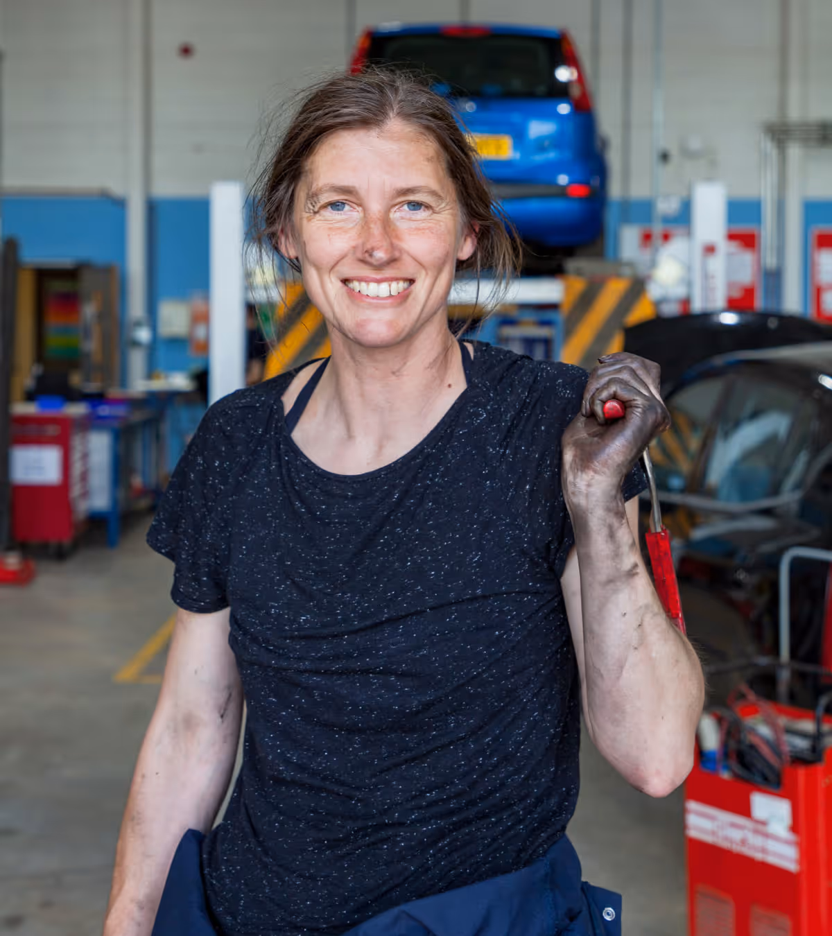 Smiling female mechanicholding a tool in an auto repair shop.